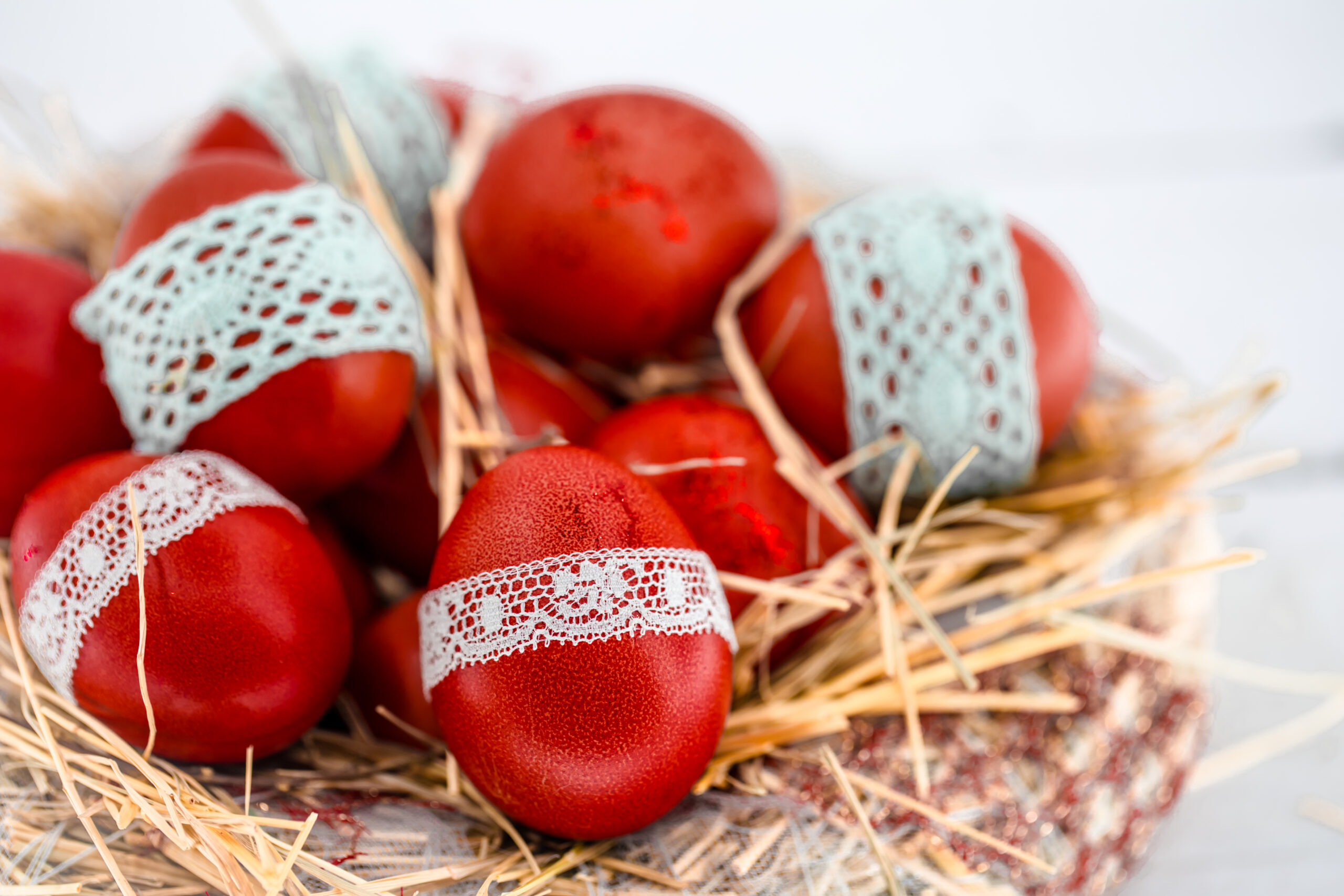 Red eggs in a nest of hay, tied a lace ribbon, close-up , lying on a white wooden background still life